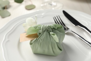 Furoshiki technique. Gift packed in green fabric with flower and blank card on table, closeup