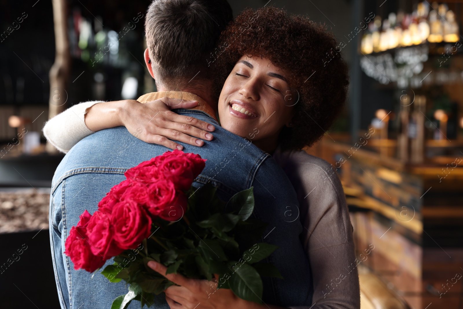 Photo of International dating. Beautiful woman with bouquet of roses hugging her boyfriend in cafe