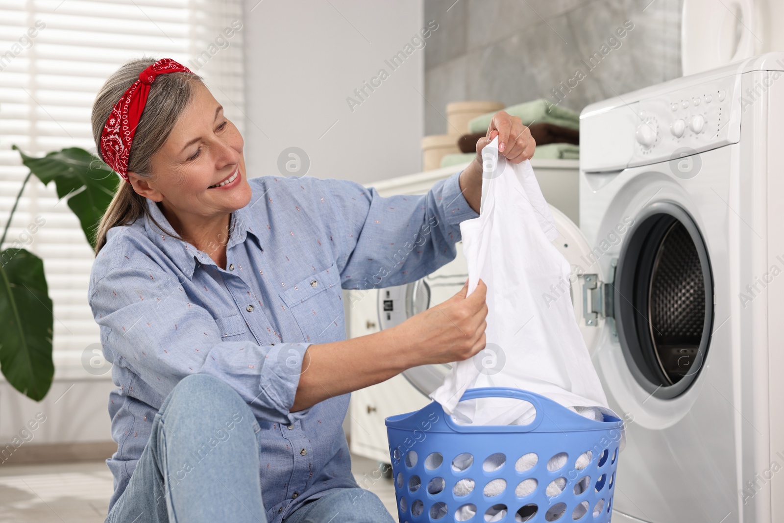 Photo of Happy housewife with laundry basket near washing machine at home