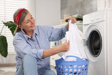 Photo of Happy housewife with laundry basket near washing machine at home