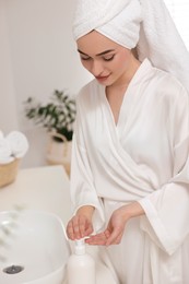 Photo of Beautiful young woman applying body cream onto hands in bathroom
