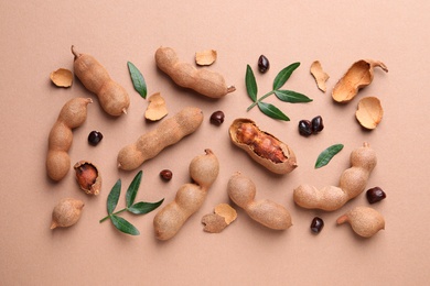 Photo of Ripe tamarinds and fresh leaves on beige background, flat lay