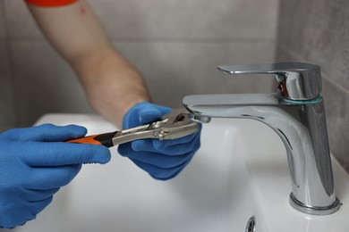 Photo of Plumber repairing faucet with spanner in bathroom, closeup