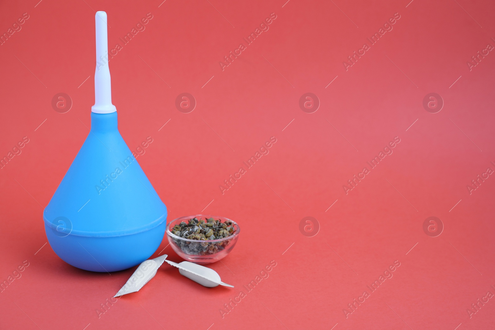 Photo of Enema, suppositories and bowl of dry chamomile on coral background, space for text