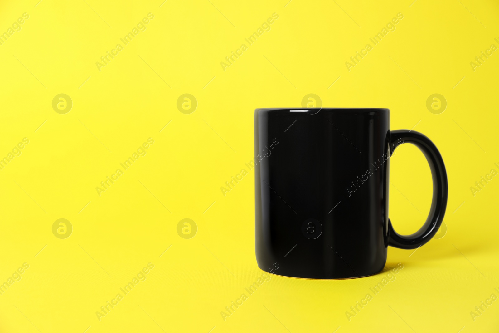 One black ceramic mug on yellow background. Space for text Photo of One black ceramic mug on yellow background. Space for text