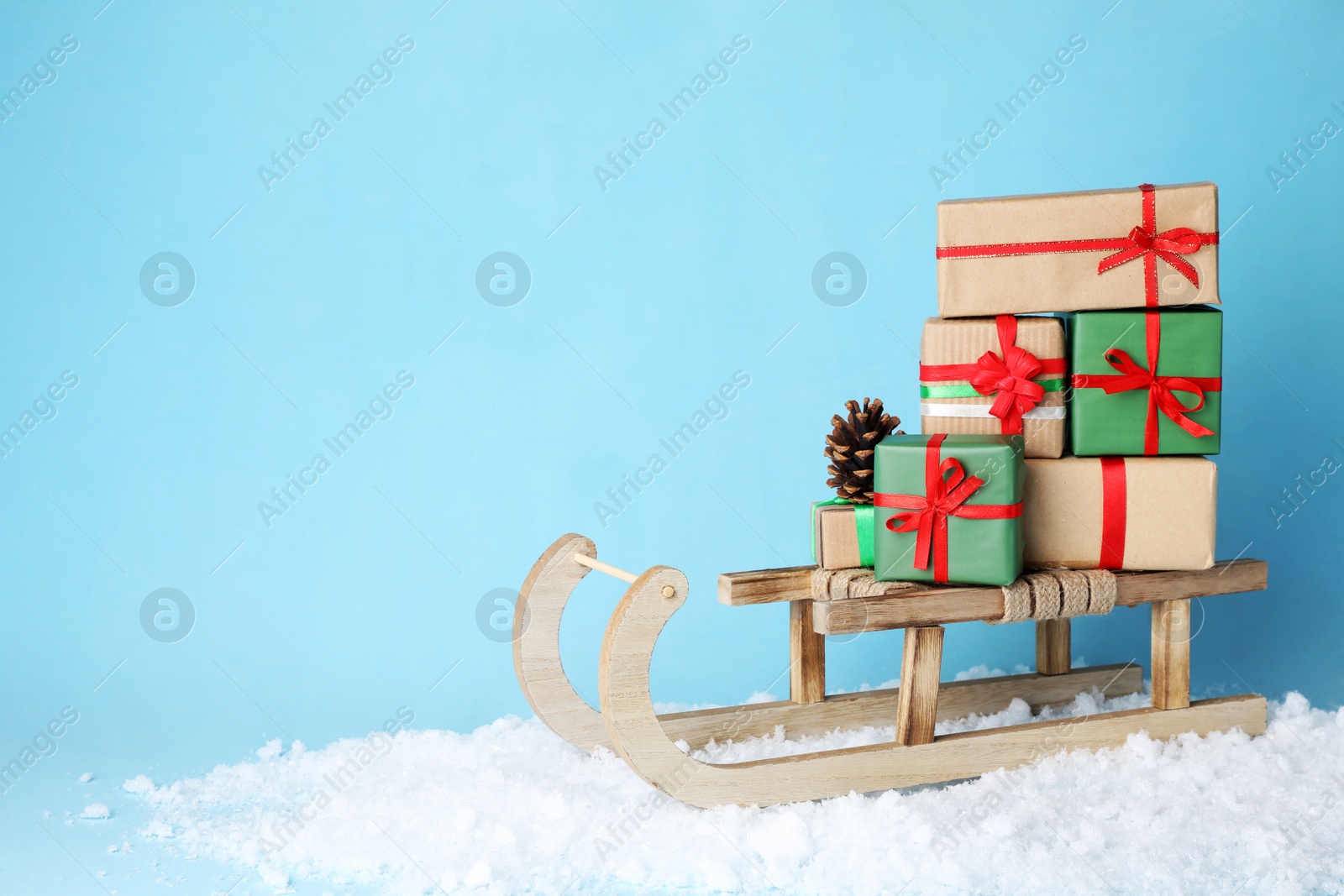 Photo of Wooden sleigh with Christmas gift boxes, pine cone and artificial snow on light blue background, space for text