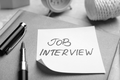 Photo of Reminder note about job interview and stationery on table, closeup