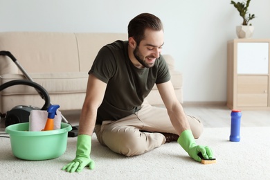 Young man cleaning carpet at home