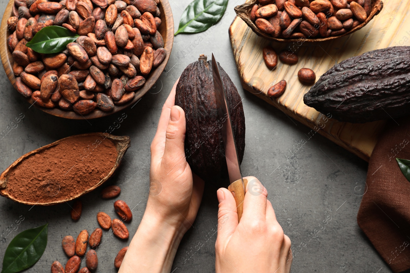 Photo of Woman cutting ripe cocoa pod over grey table with products, top view