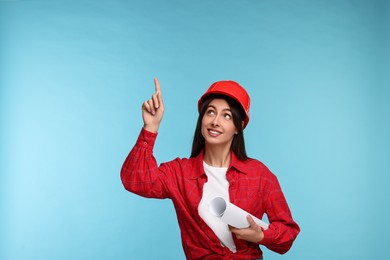 Photo of Architect in hard hat with draft pointing at something on light blue background