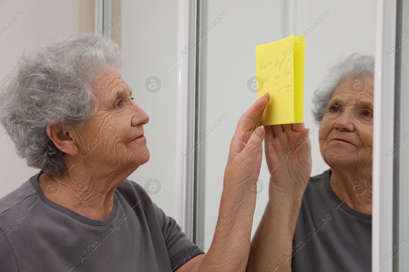 Photo of Senior woman looking at reminder note indoors. Age-related memory impairment