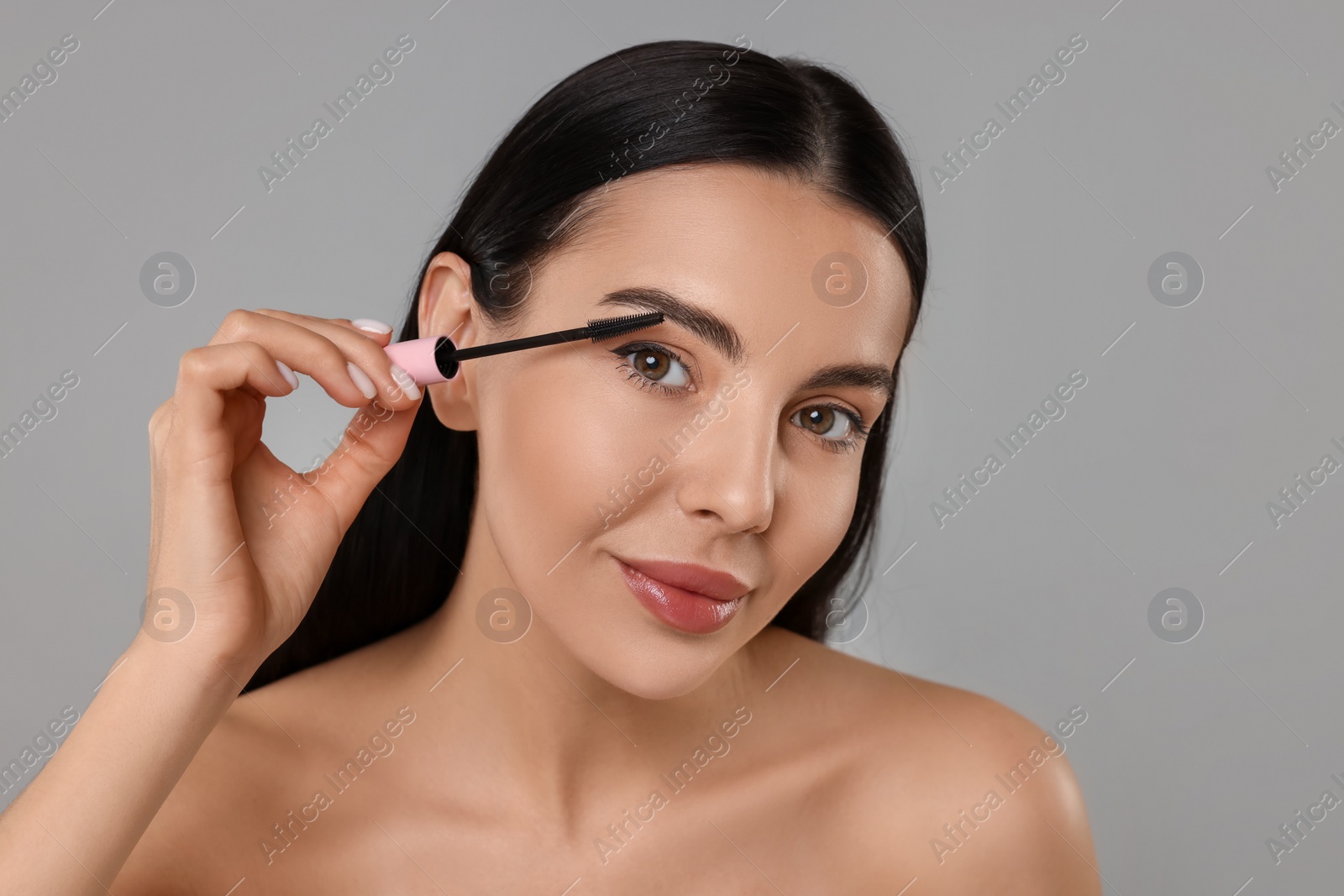 Photo of Beautiful young woman applying mascara on grey background