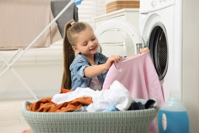 Little girl taking out dirty clothes from basket in bathroom