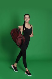 Beautiful woman with sports bag on green background