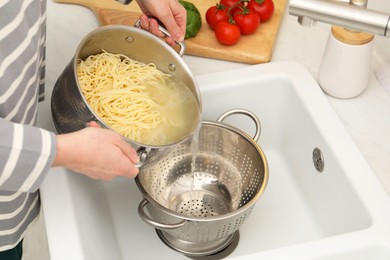 Photo of Woman draining pasta into colander at sink, closeup