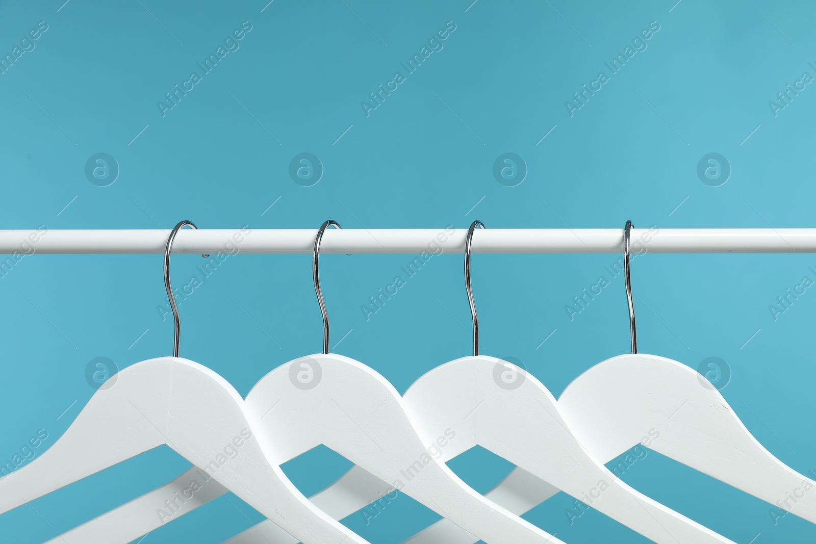 Photo of Empty clothes hangers on rack against light blue background, closeup