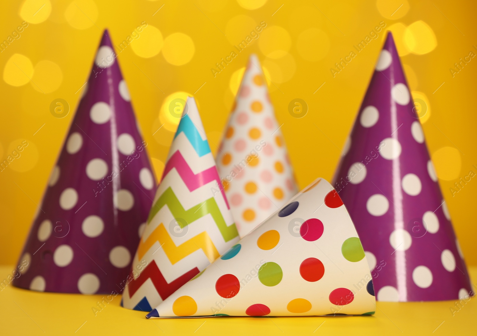 Photo of Beautiful party hats on yellow table against blurred festive lights