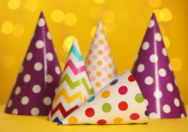 Beautiful party hats on yellow table against blurred festive lights