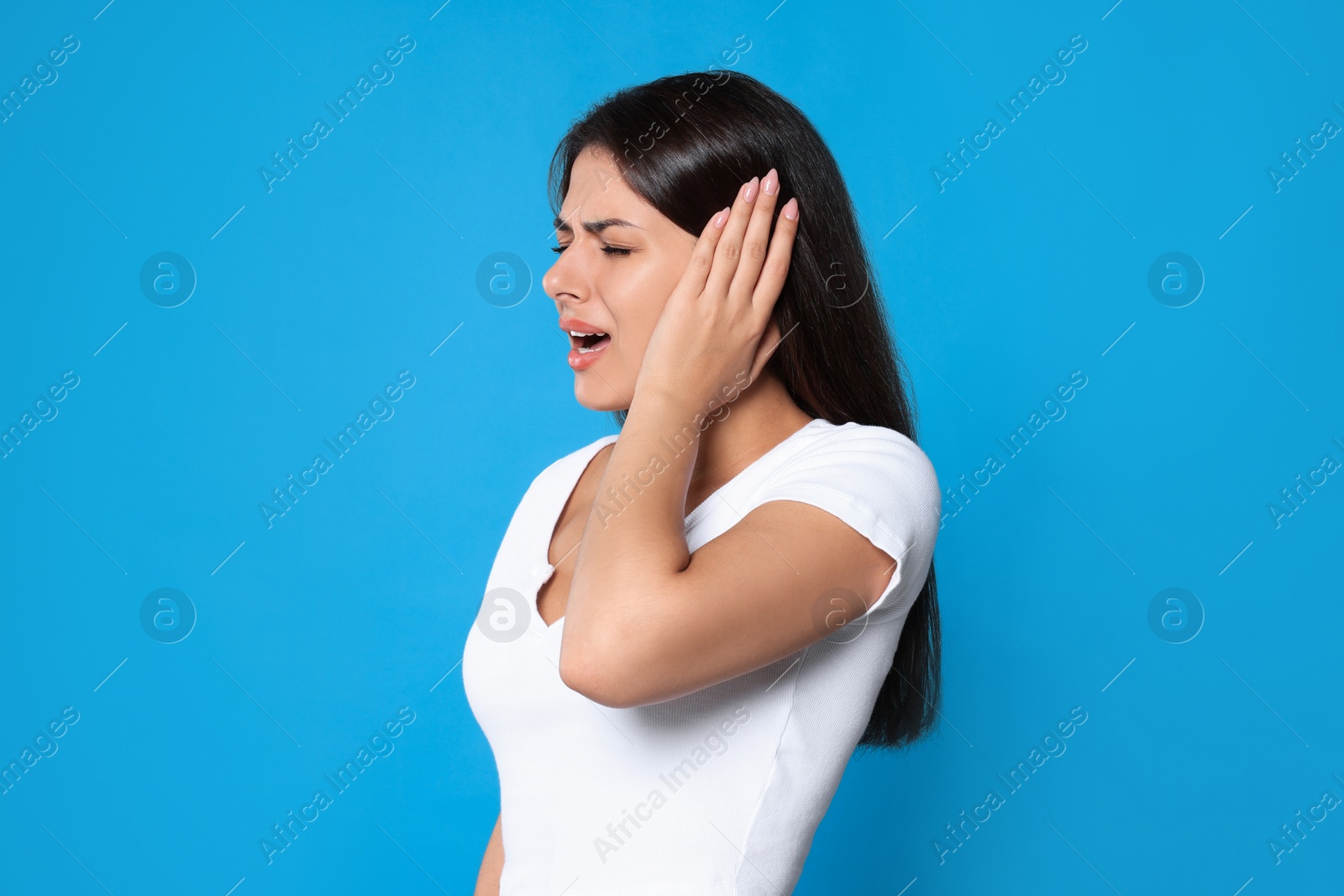 Photo of Young woman suffering from ear pain on light blue background