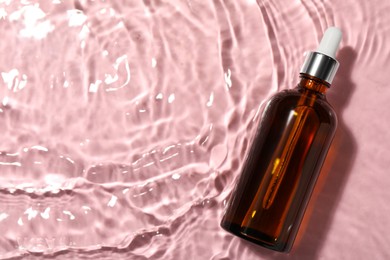 Photo of Bottle of hydrophilic oil in water on pink background, top view. Space for text