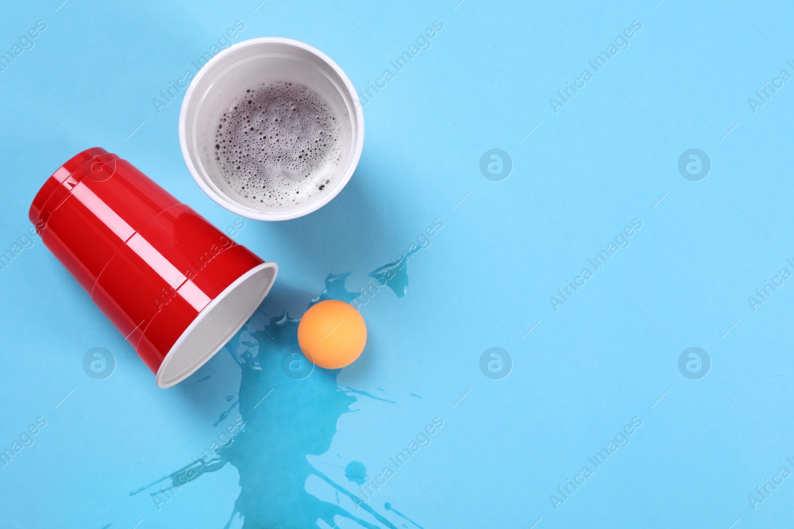 Photo of Plastic cups and ball on light blue background, flat lay. Beer pong game