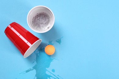 Plastic cups and ball on light blue background, flat lay. Beer pong game