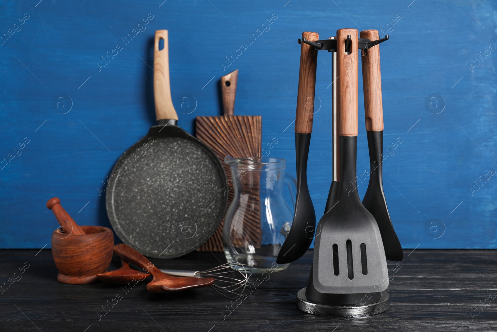 Photo of Set of different kitchen utensils on black table against blue wooden background