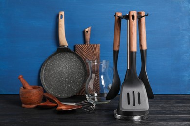 Set of different kitchen utensils on black table against blue wooden background