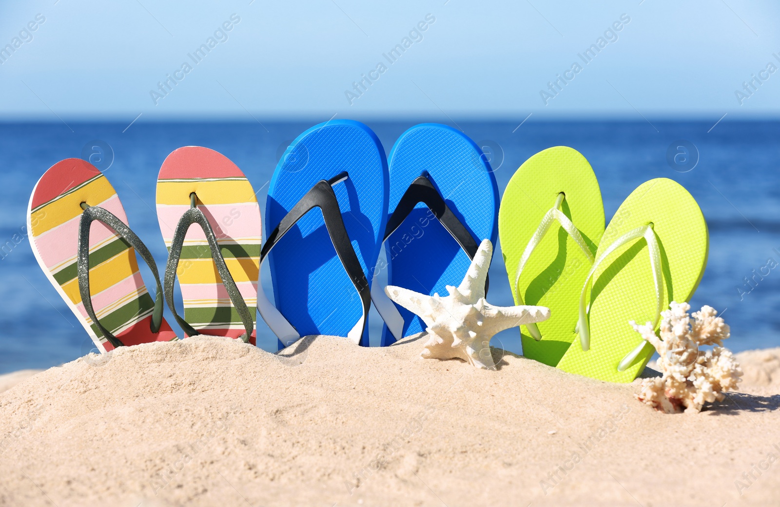 Photo of Composition with bright flip flops on sand near sea in summer. Beach accessories