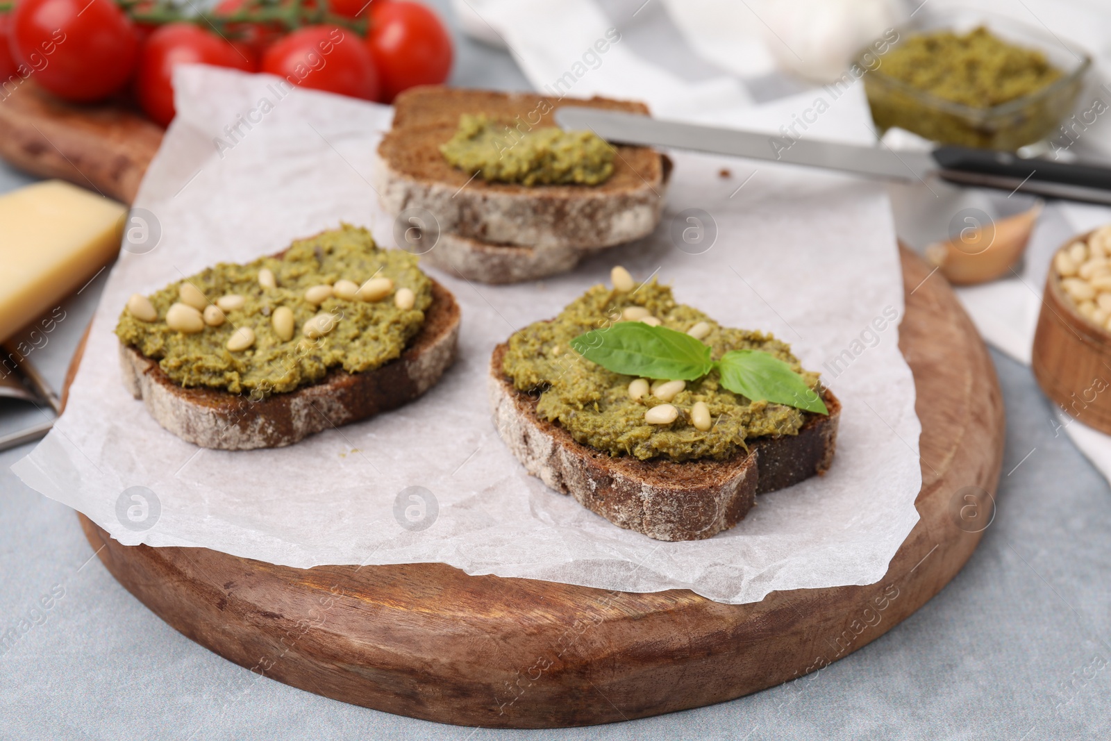 Photo of Tasty bruschettas with pesto sauce, nuts and fresh basil on light grey table, closeup