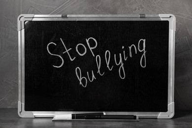 Photo of Chalkboard with phrase Stop Bullying on table near grey wall