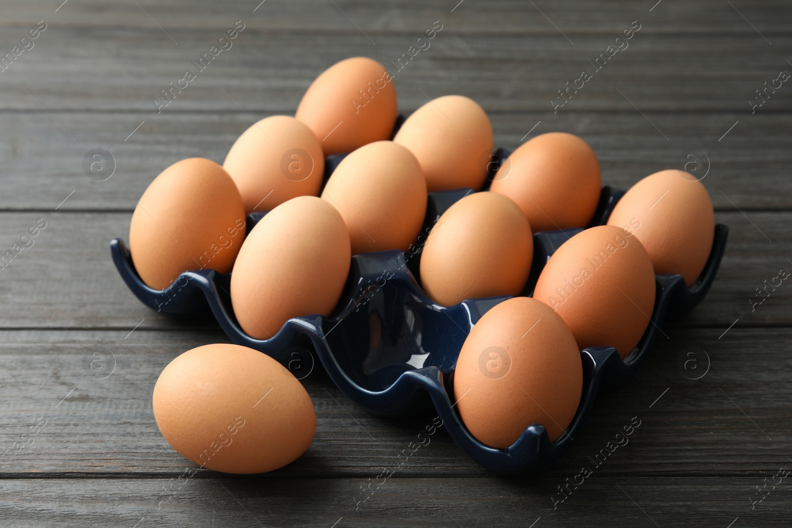 Photo of Raw chicken eggs in ceramic holder on wooden background