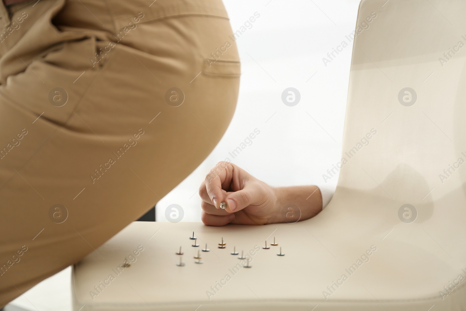 Photo of Man putting pins on chair while his colleague sitting down, closeup. April fool's day