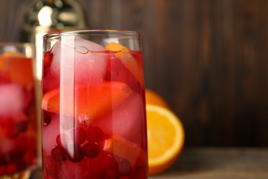 Photo of Tasty cranberry cocktail with ice cubes and orange in glass on table, closeup. Space for text