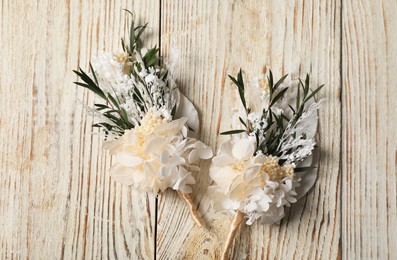 Stylish boutonnieres on light wooden table, top view