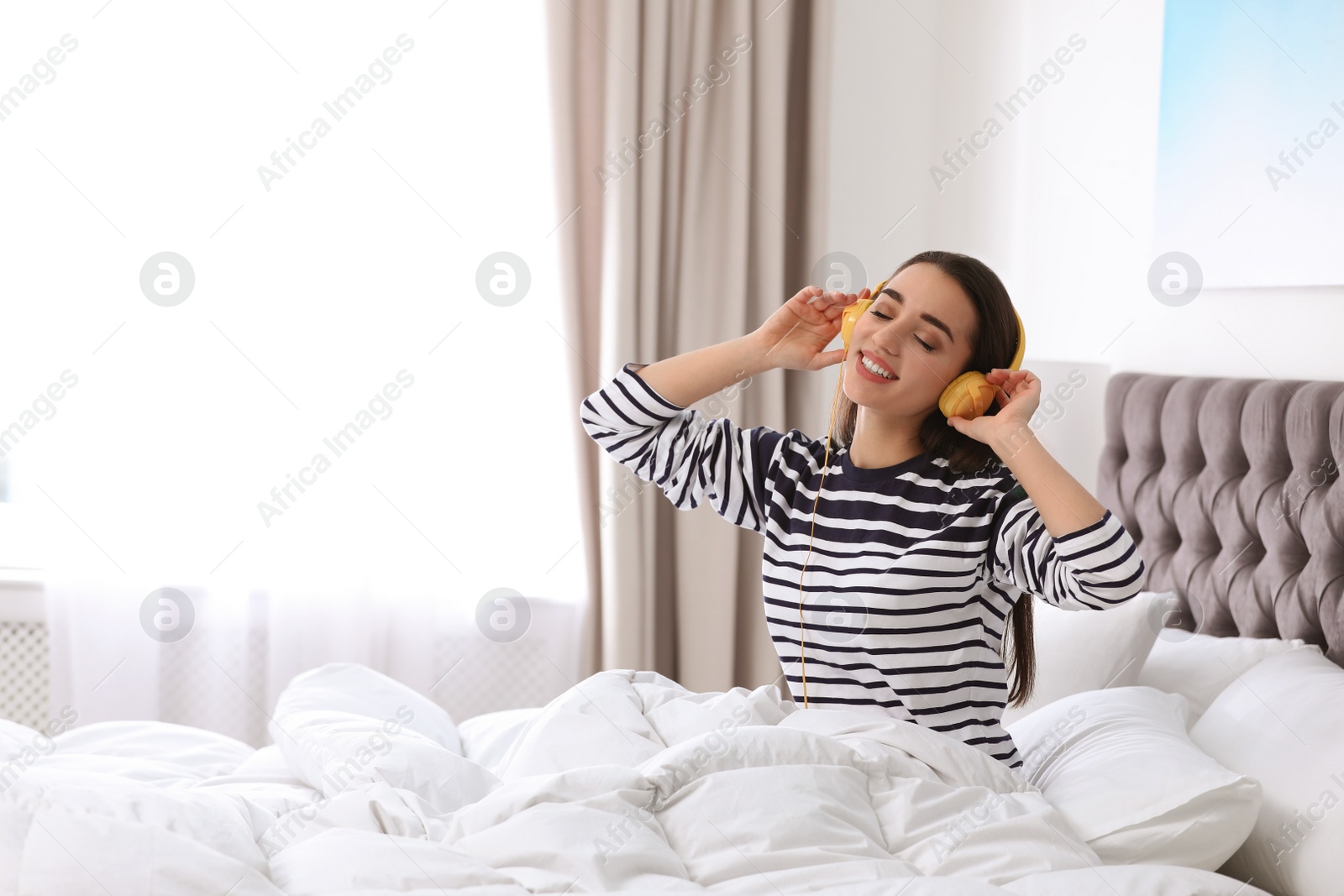 Photo of Young woman with headphones enjoying music in bed