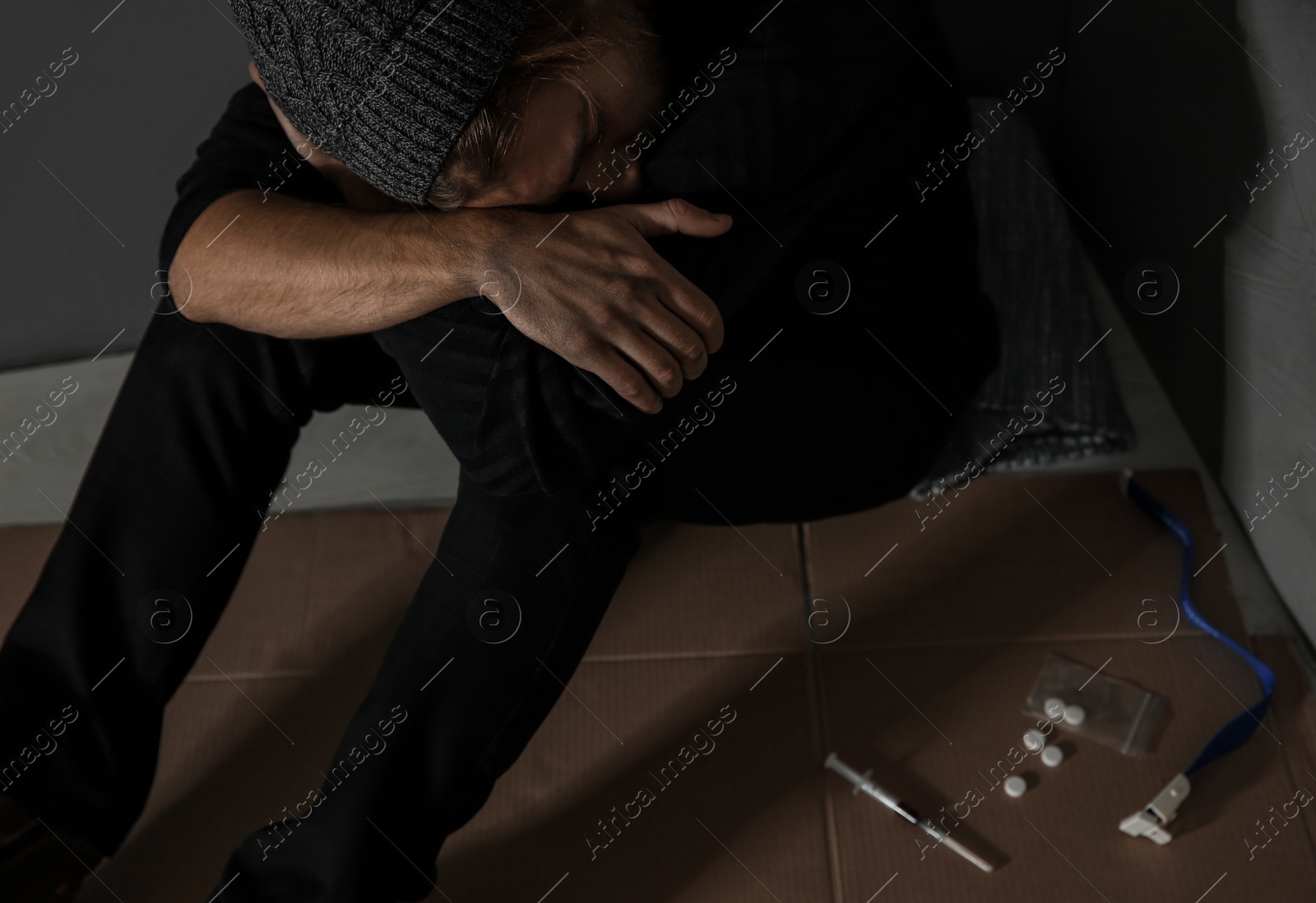 Photo of Stoned drug addict sitting on floor near grey wall