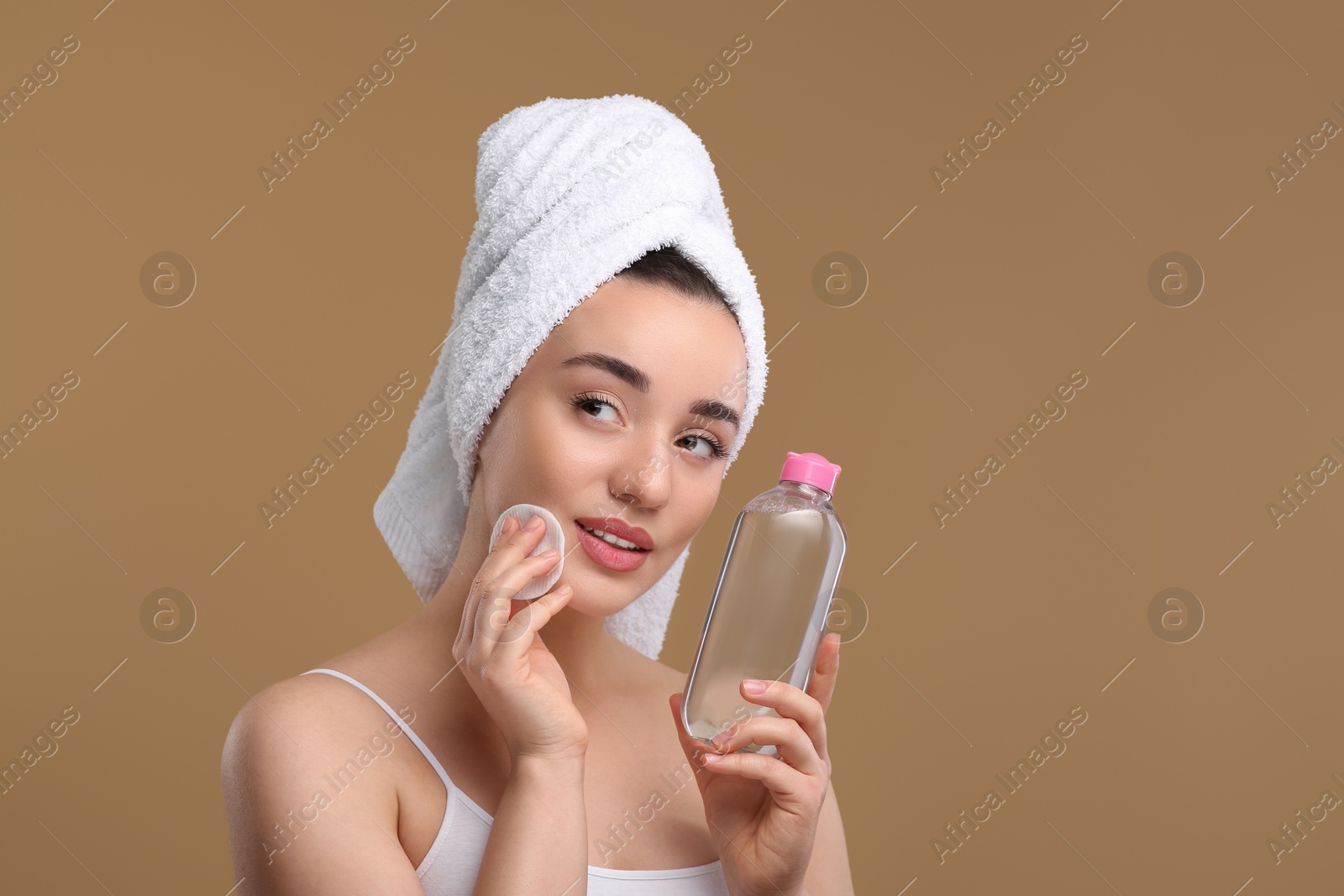 Photo of Beautiful woman in terry towel removing makeup with cotton pad on beige background, space for text