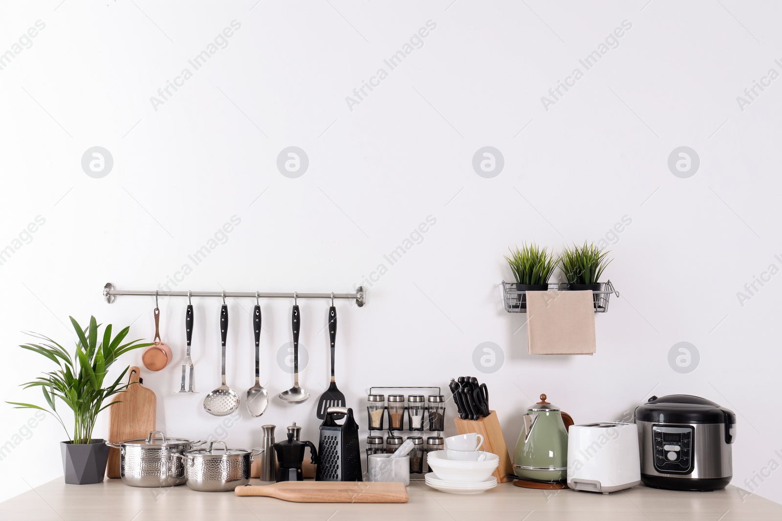 Photo of Set of clean cookware, dishes, utensils and appliances on table at white wall