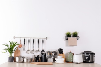 Photo of Set of clean cookware, dishes, utensils and appliances on table at white wall