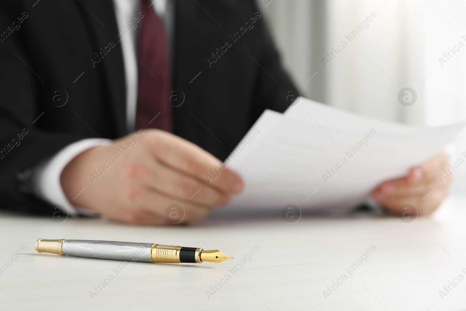 Photo of Notary reading documents at wooden table, focus on fountain pen