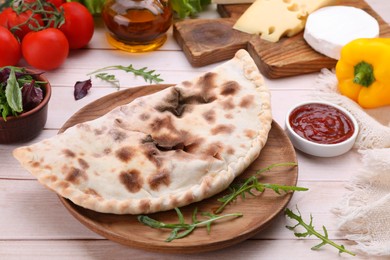 Photo of Delicious calzone and products on light wooden table