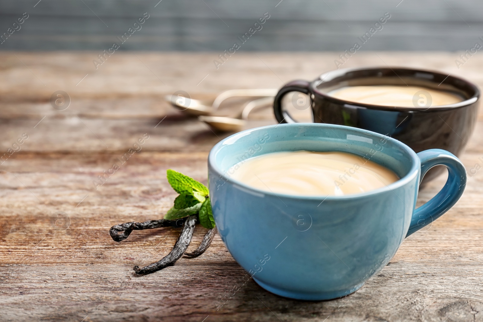 Photo of Cups with vanilla pudding, sticks and fresh mint on wooden table