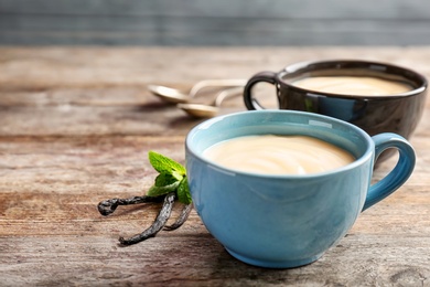 Cups with vanilla pudding, sticks and fresh mint on wooden table