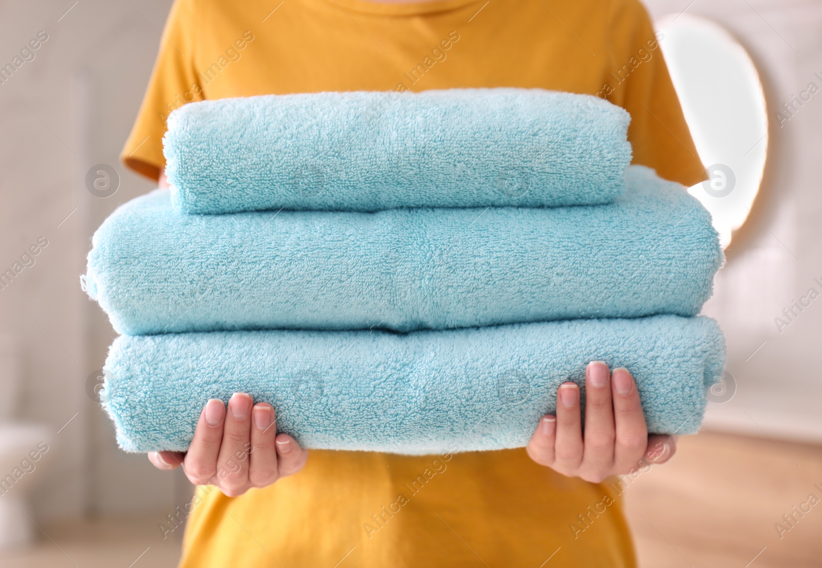 Photo of Woman holding stack of fresh towels indoors, closeup