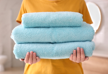 Woman holding stack of fresh towels indoors, closeup