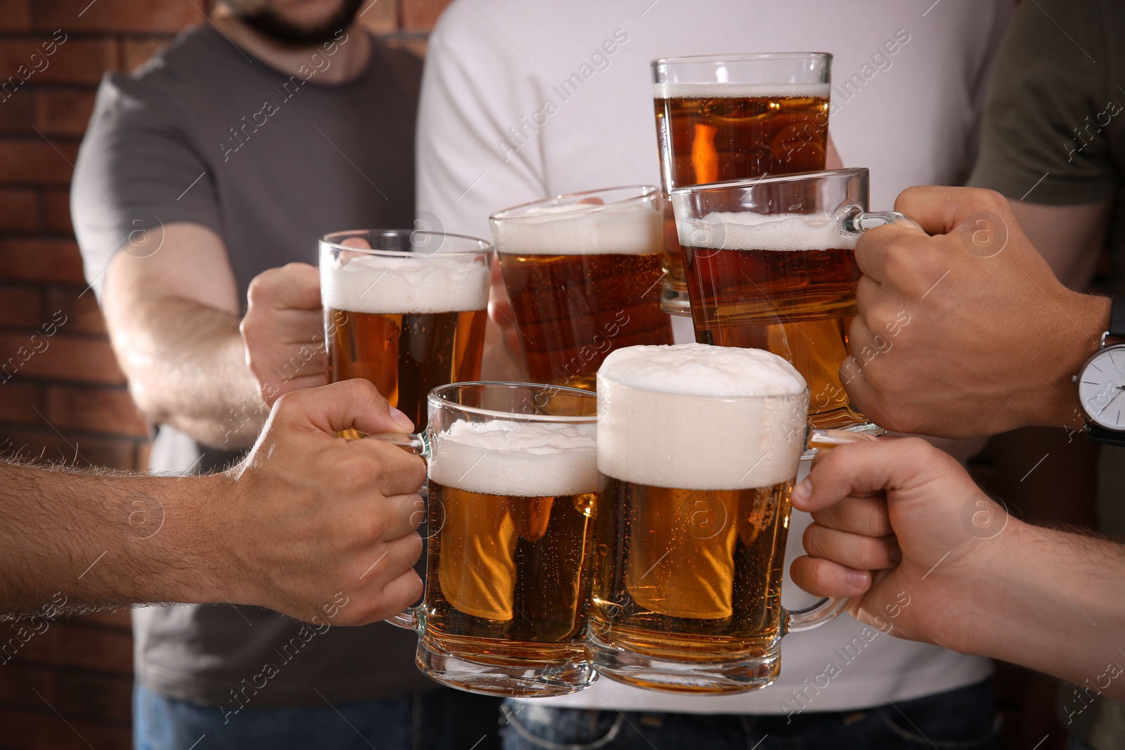 Photo of Friends clinking glasses of beer near red brick wall, closeup