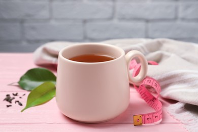 Photo of Cup of herbal diet tea and measuring tape on pink wooden table against brick wall, closeup. Weight loss concept