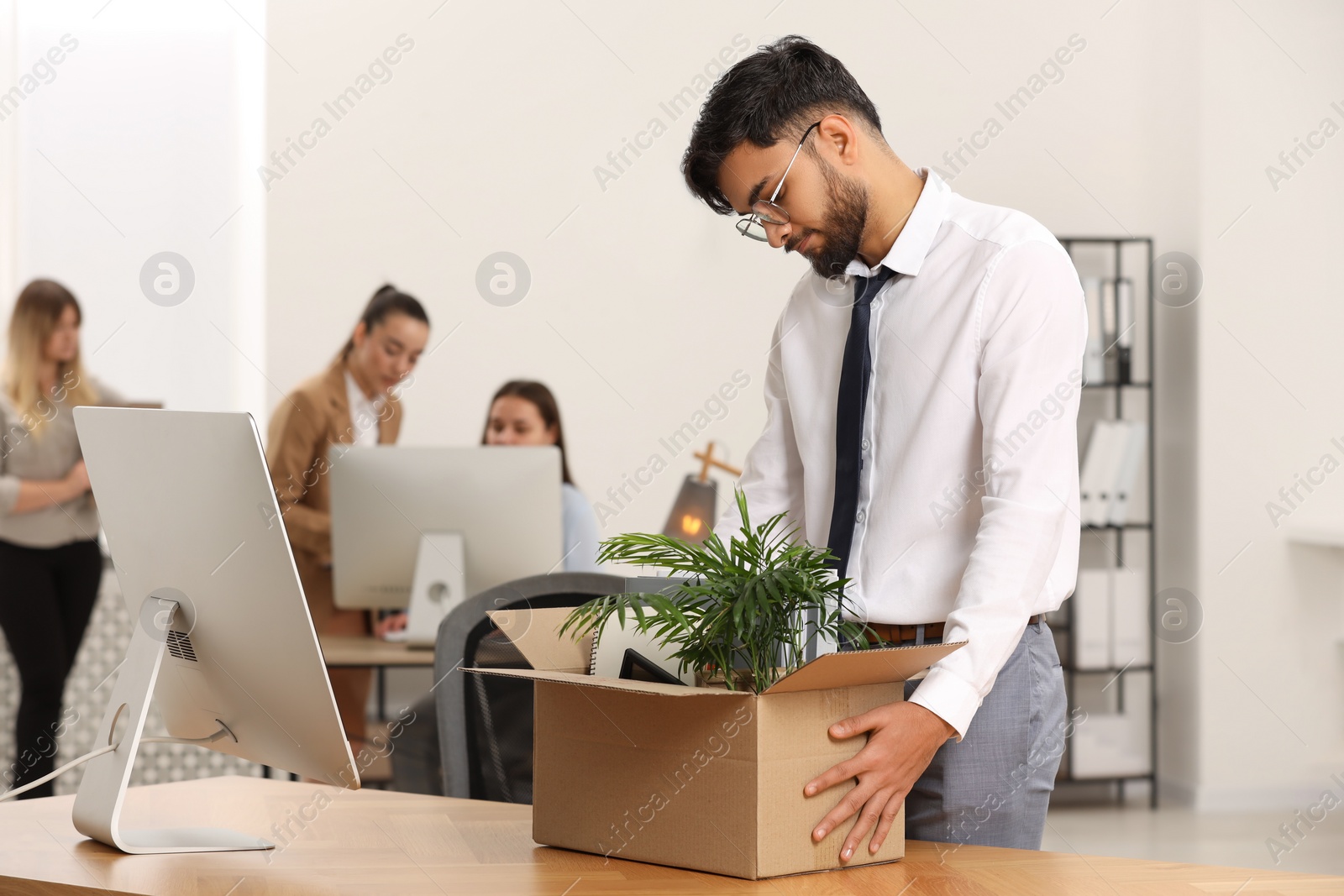 Photo of Unemployment problem. Frustrated man with box of personal belongings at table in office