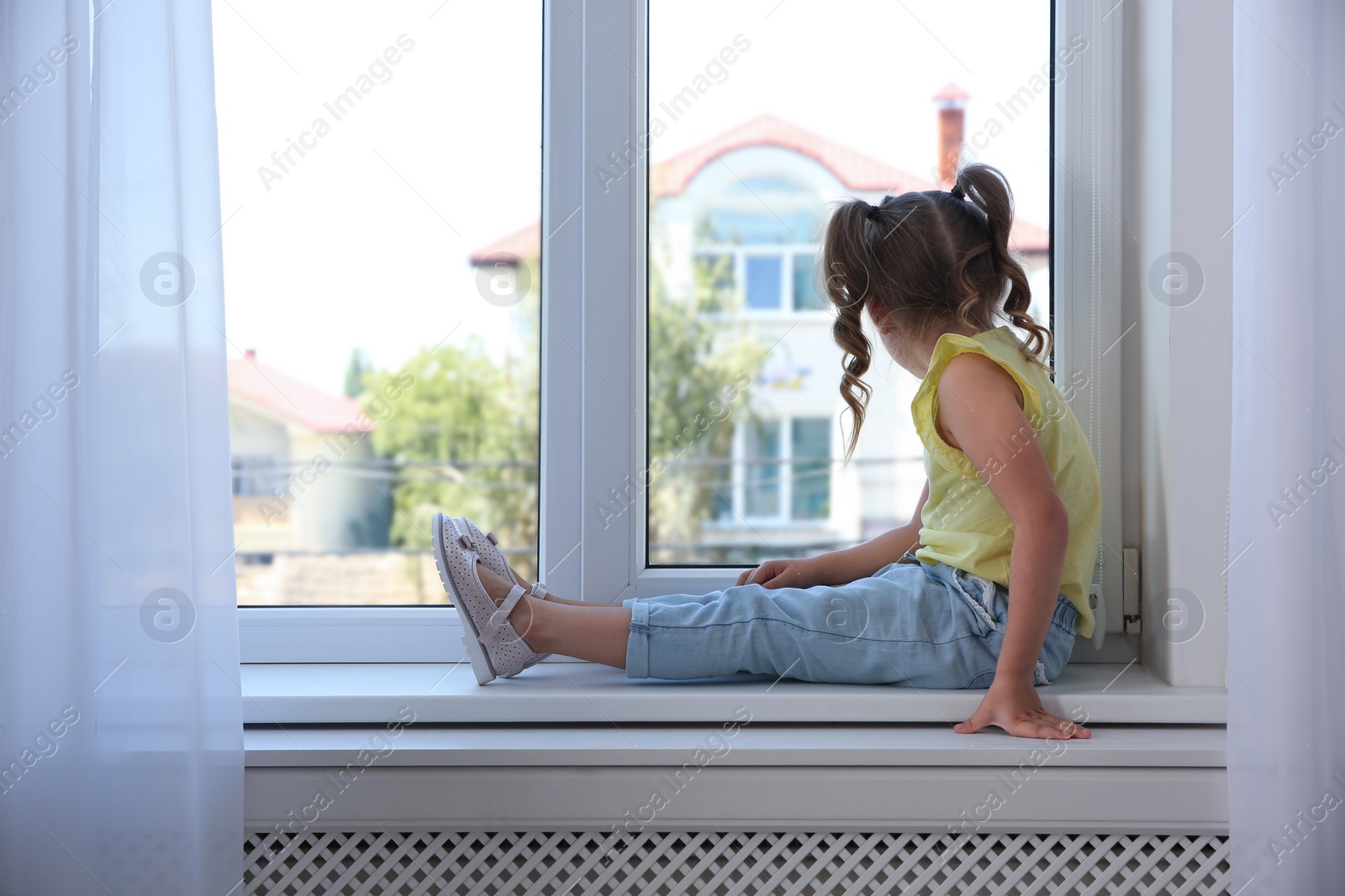 Photo of Cute little girl on window sill at home